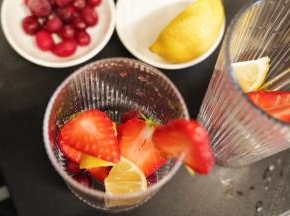 在杯里勺入30克椰果粒，柠檬洗净后切成小块放入杯里，把切好的草莓和蔓越莓鲜果也放入杯中