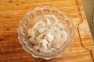 虾仁去除虾线，洗净后放入碗里，加入生粉和2克盐抓拌均匀腌制10分钟