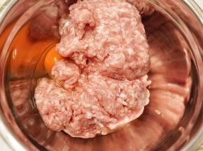 把猪肉糜放入料理盆里，磕入一个鸡蛋，把鸡蛋搅拌至完全被猪肉吸收