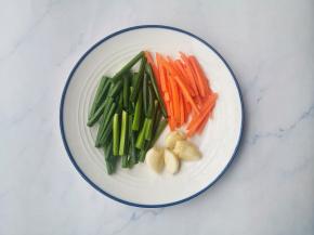 韭苗洗净切段，胡萝卜去皮切段，大蒜拍扁。