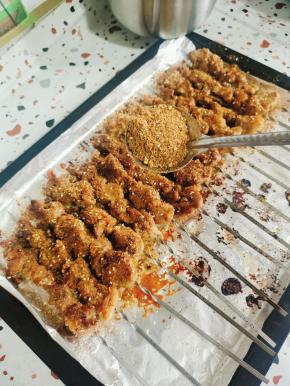 把烤盘取出来，用漏勺在肉串上撒适量的烧烤料！撒好一面，把肉串翻面，再继续均匀的撒烧烤料！