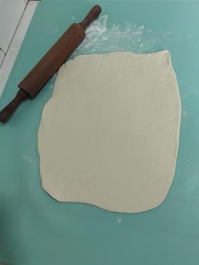用擀面杖把面团压扁，再擀！先去给它擀四个角！四个角擀完，往长擀，往宽擀！擀成一个长方形！