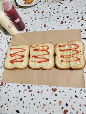 把加厚小熊包装纸平铺在干燥的案板上，准备三片切好的面包片！挤上适量的沙拉酱和番茄酱！