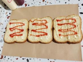 把加厚小熊包装纸平铺在干燥的案板上，准备三片切好的面包片！挤上适量的沙拉酱和番茄酱！