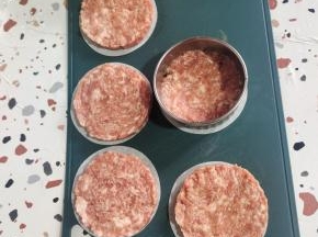 烤盘上放一张烤肉纸，饺子皮模具放在烤肉纸上，挖两勺腌制好的肉馅儿。按压成圆饼状！